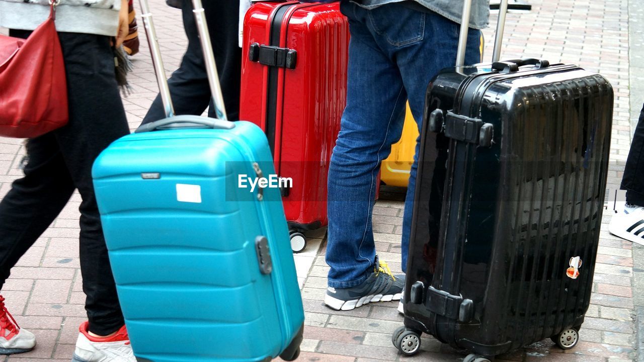 Low section of people with wheeled luggage on footpath