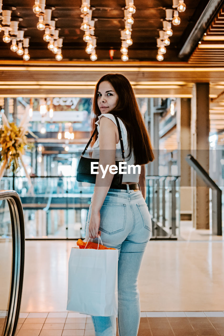 Young brunette latina attractive woman with shopping bags on escalator in the fashion store mall.