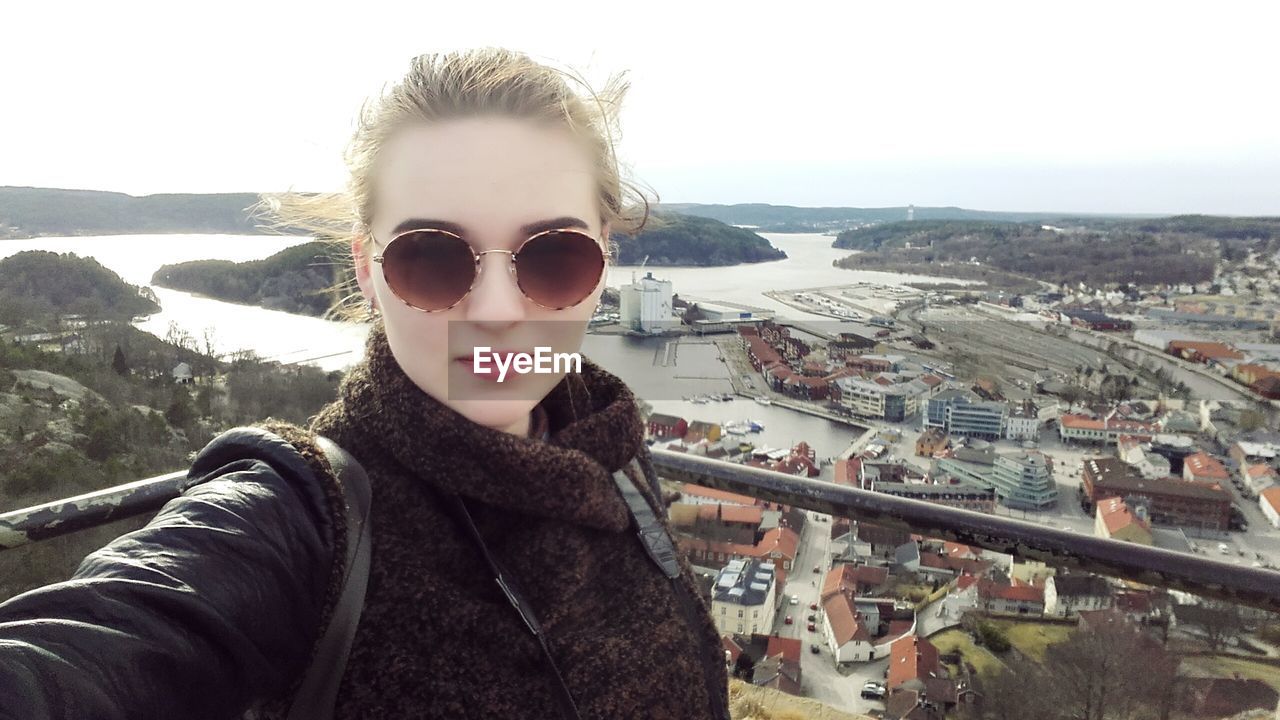 PORTRAIT OF YOUNG WOMAN WITH SUNGLASSES AGAINST SKY