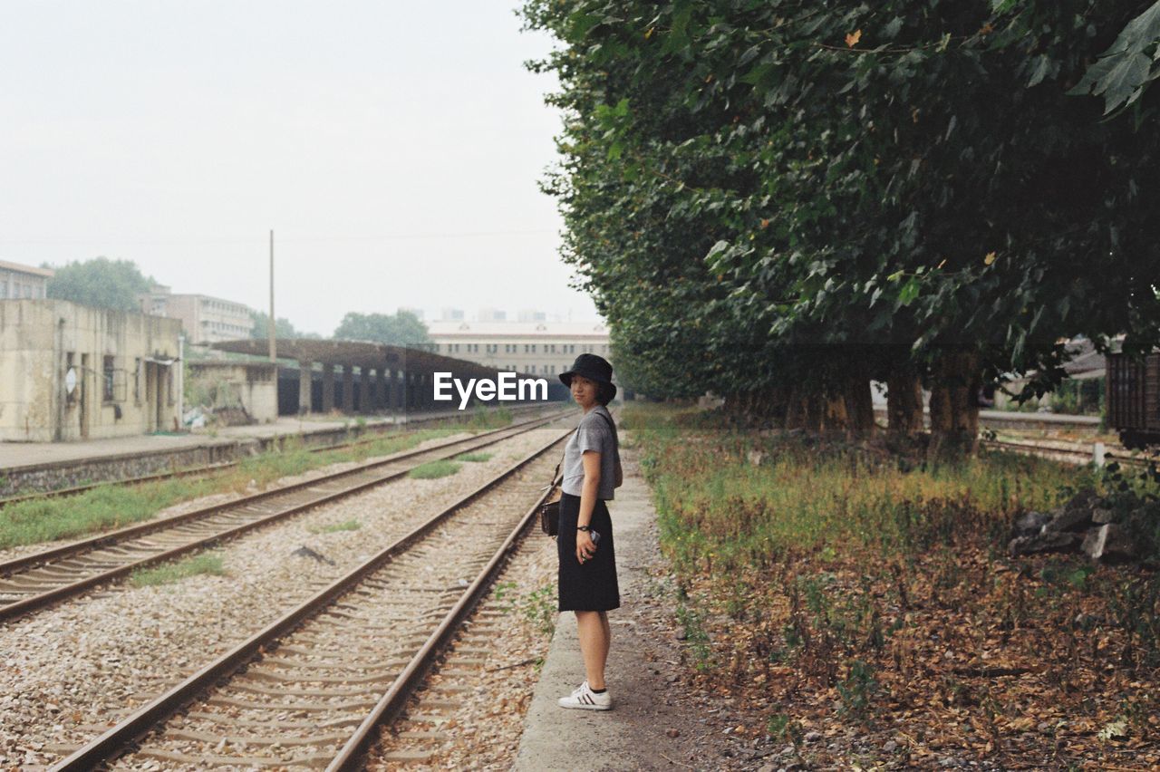 REAR VIEW OF WOMAN WALKING ON RAILROAD TRACKS