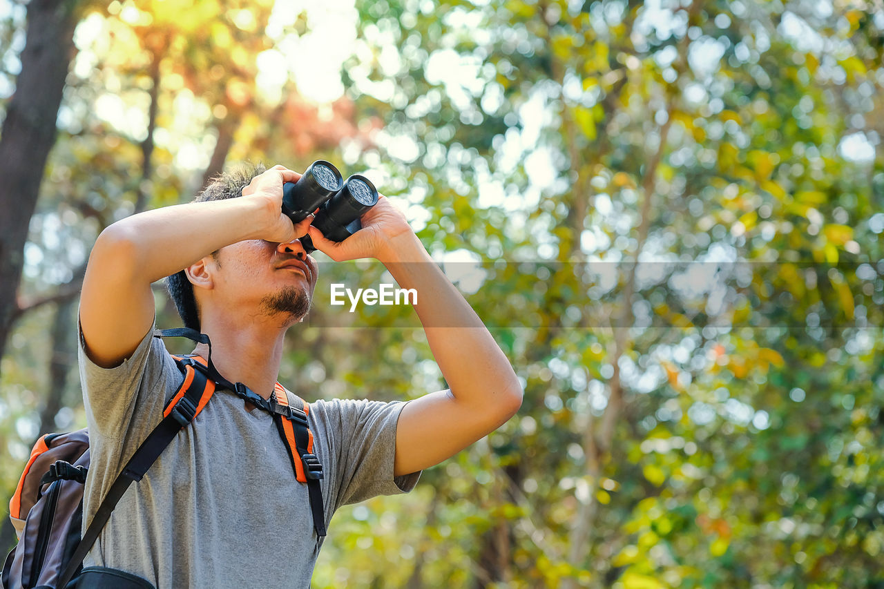 Man looking through binocular at forest