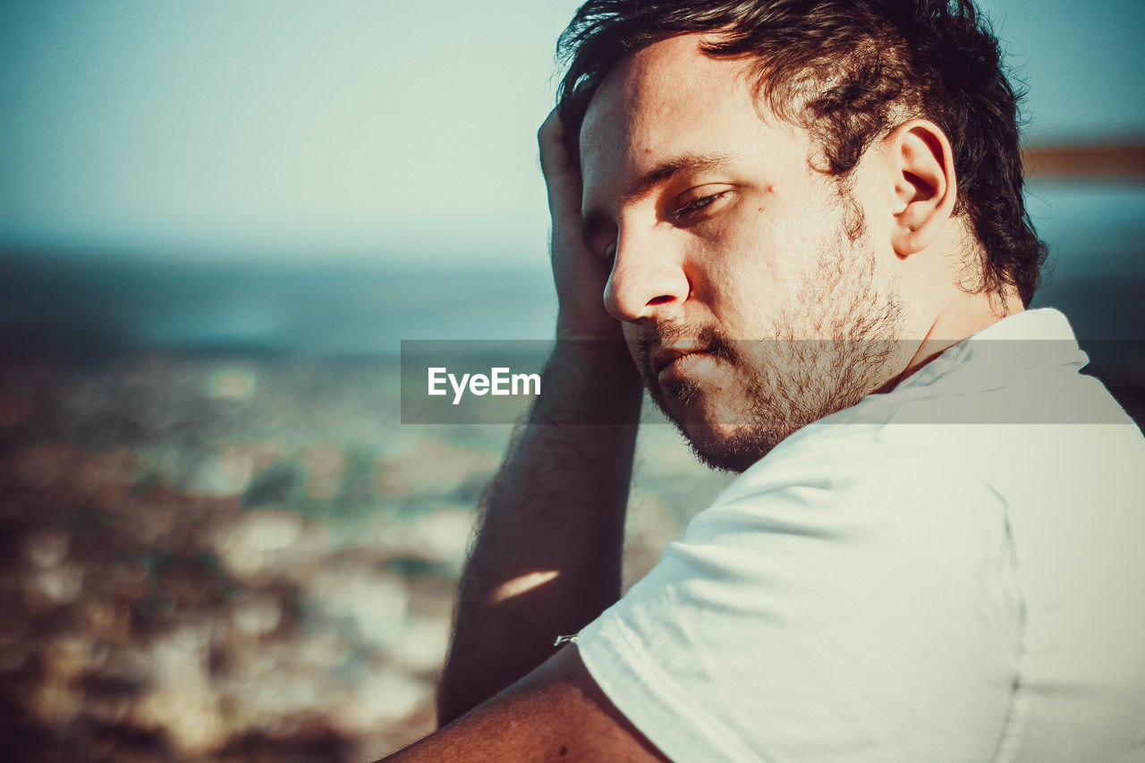 Close-up of thoughtful young man against sky