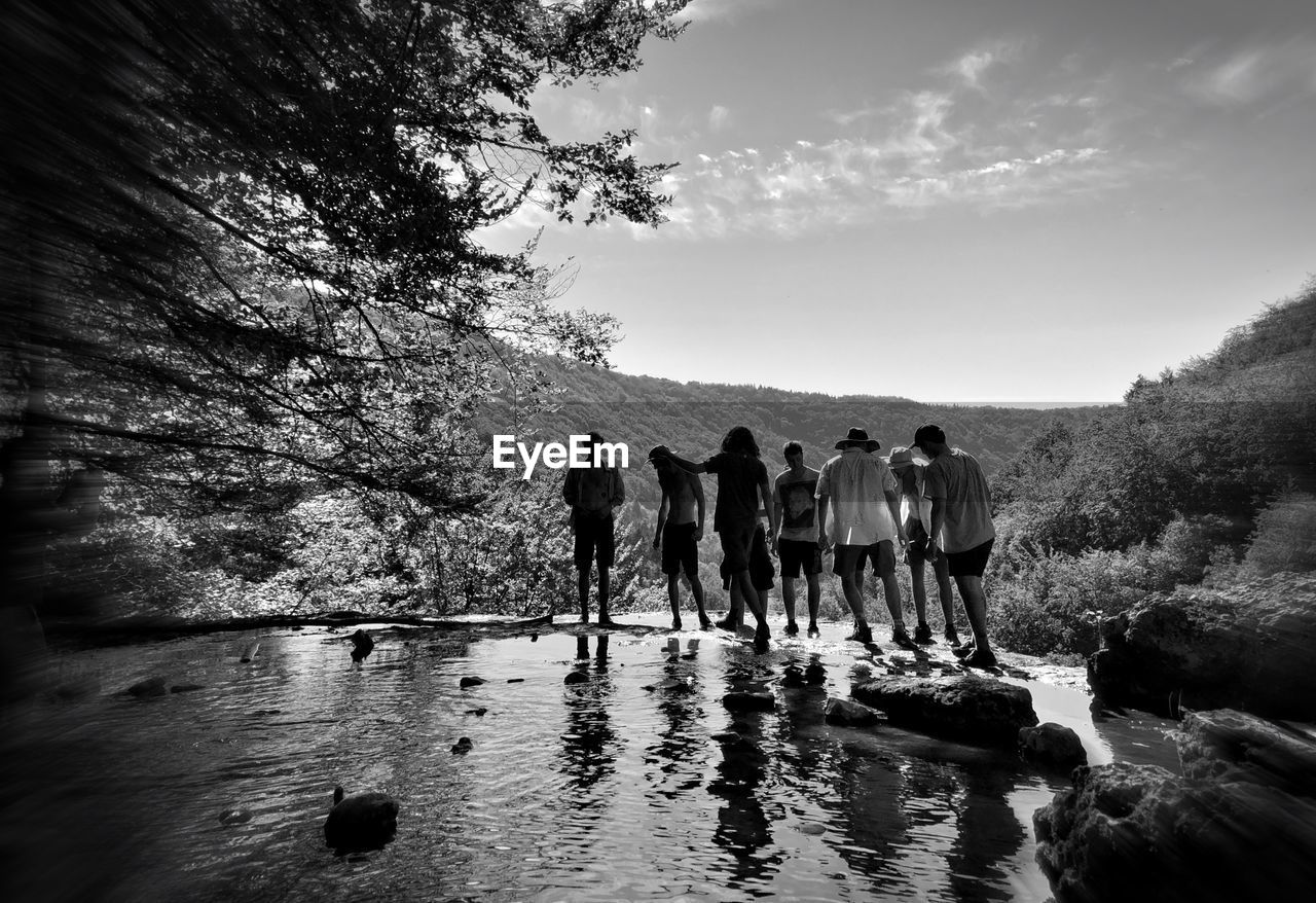 PEOPLE STANDING ON LAKE AGAINST SKY