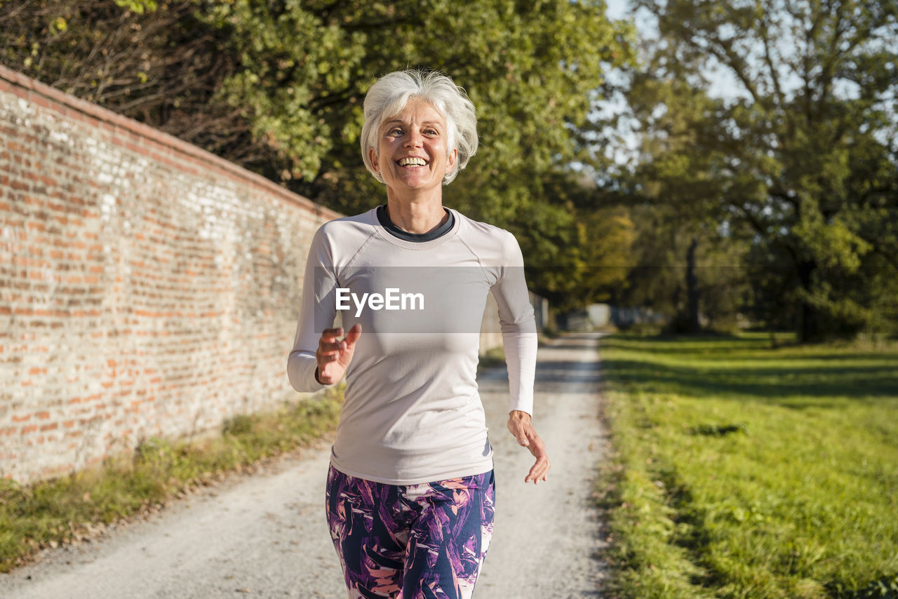 Happy senior woman running along brick wall in a park