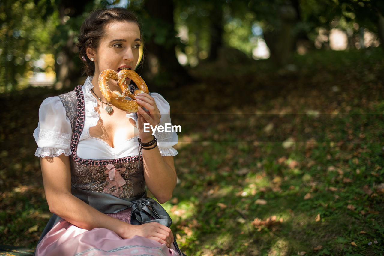 Woman eating pretzel while sitting on field