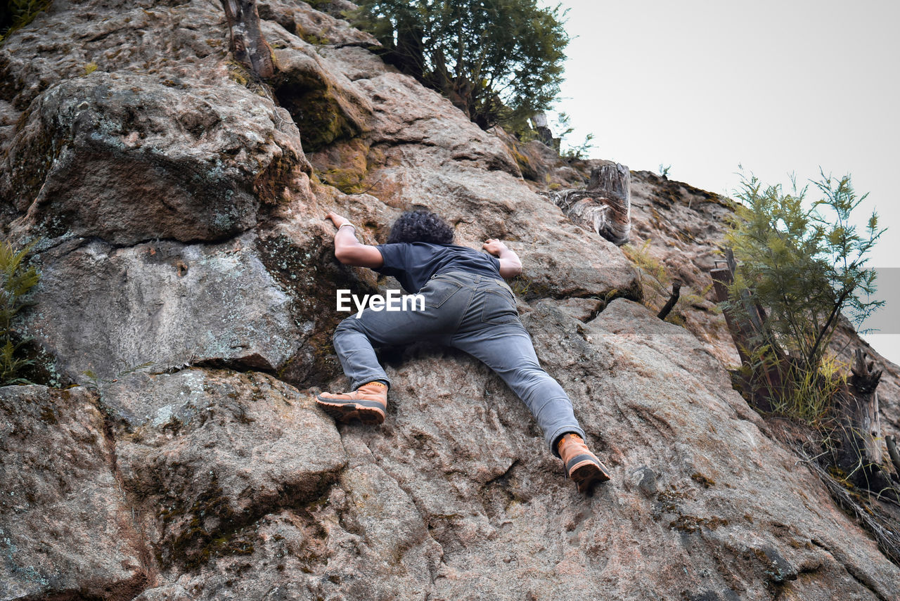 Full length rear view of man climbing on rock against clear sky