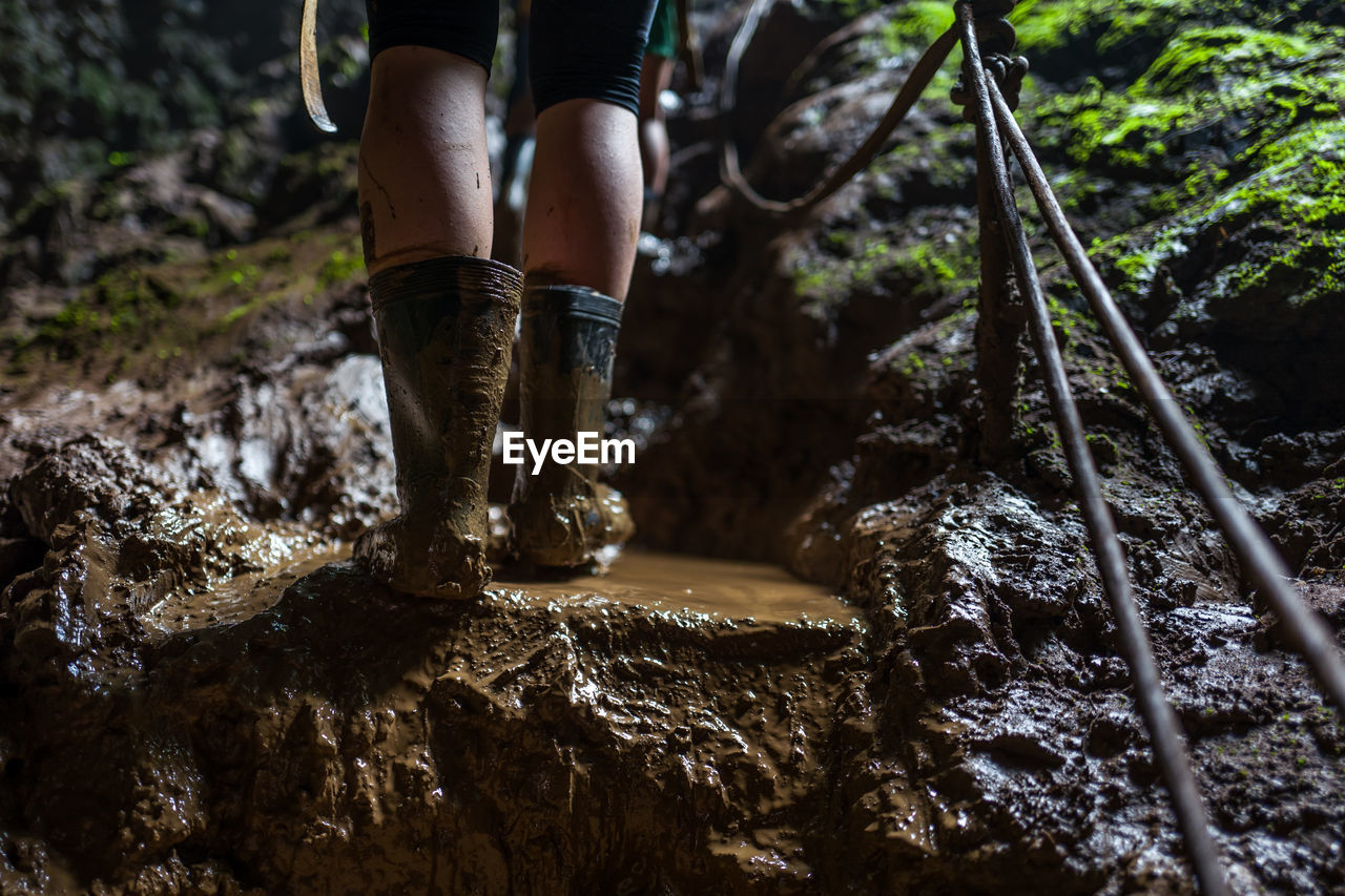 Low section of woman wearing muddy rubber boots while standing on rock in forest