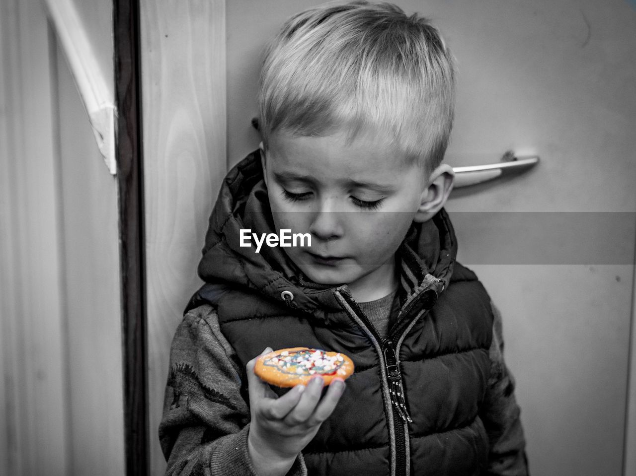 Cute boy holding cookie while standing against door at home