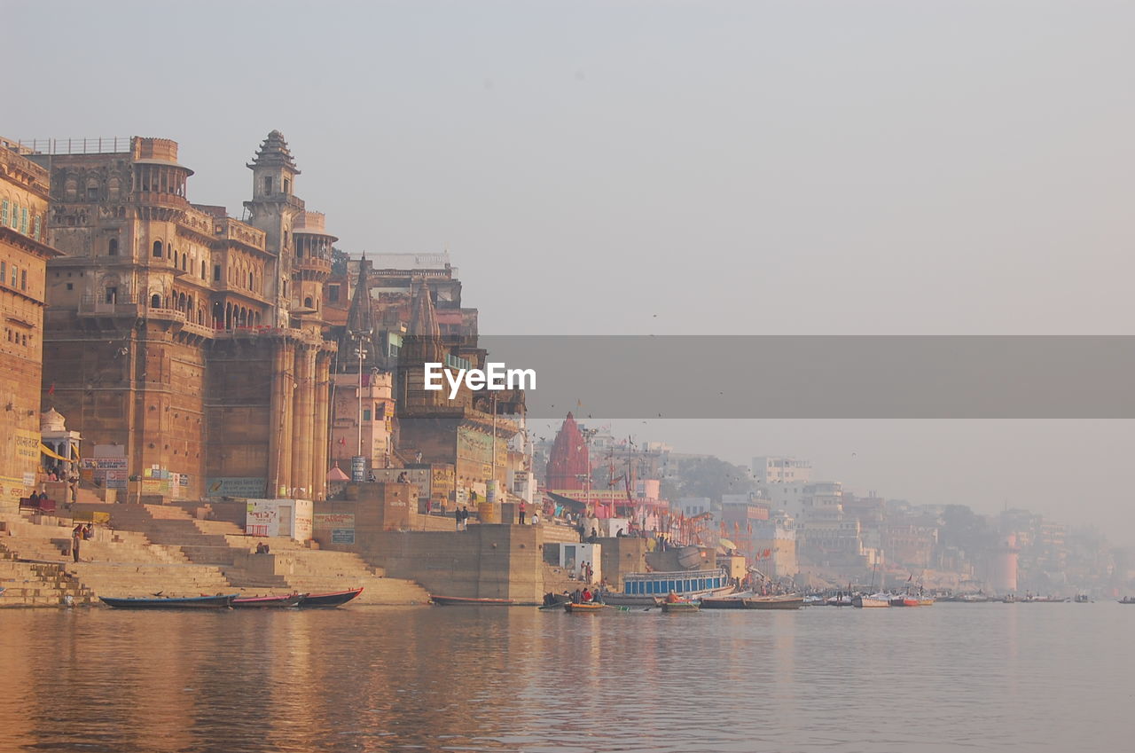 Temples by ganges river against sky during foggy weather