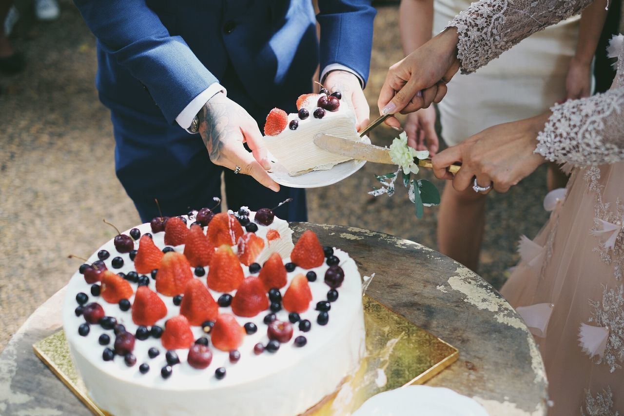 Close-up of hands cutting wedding cake