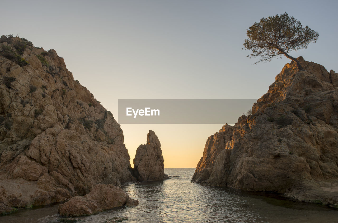 Rock formations by sea against clear sky