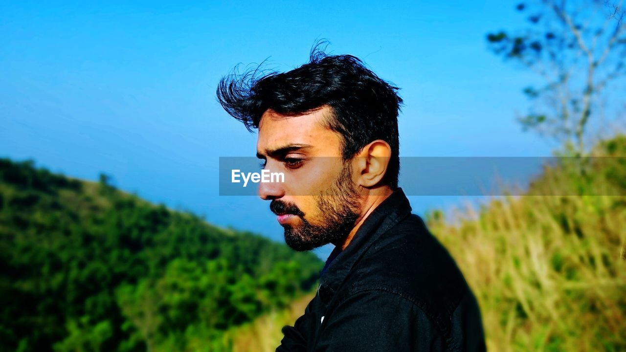 Side view of handsome bearded man standing against clear blue sky