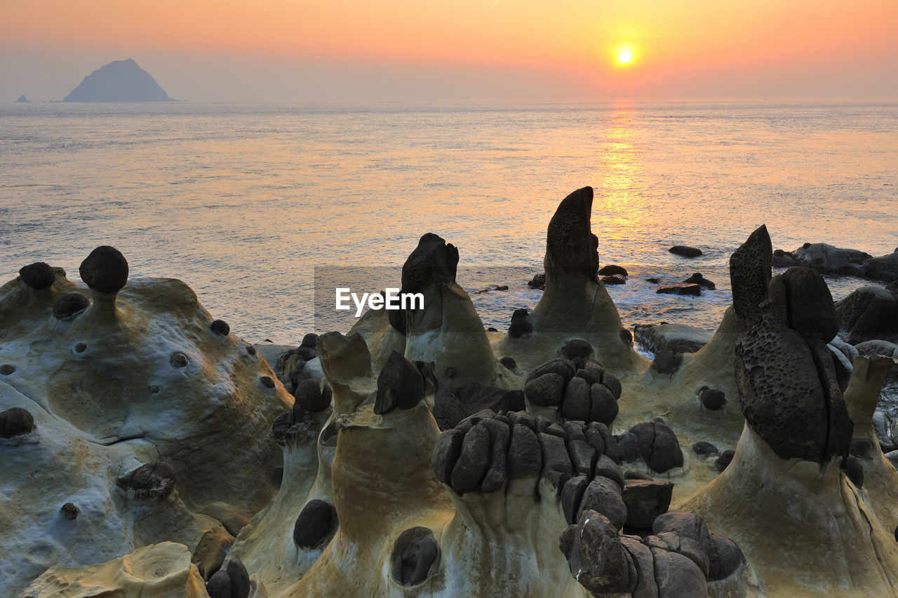 Rock formations by sea against sky at sunset