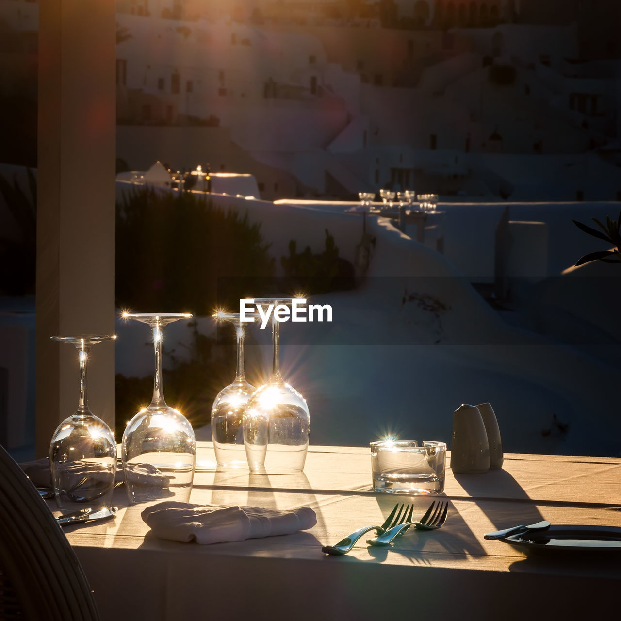 Restaurant table decorated with glasses on terrace in sunset light on the island santorini, greece