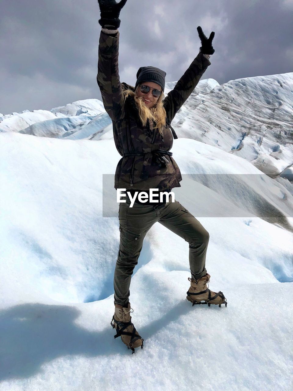 Portrait of woman with arms raised standing against snowcapped mountains 