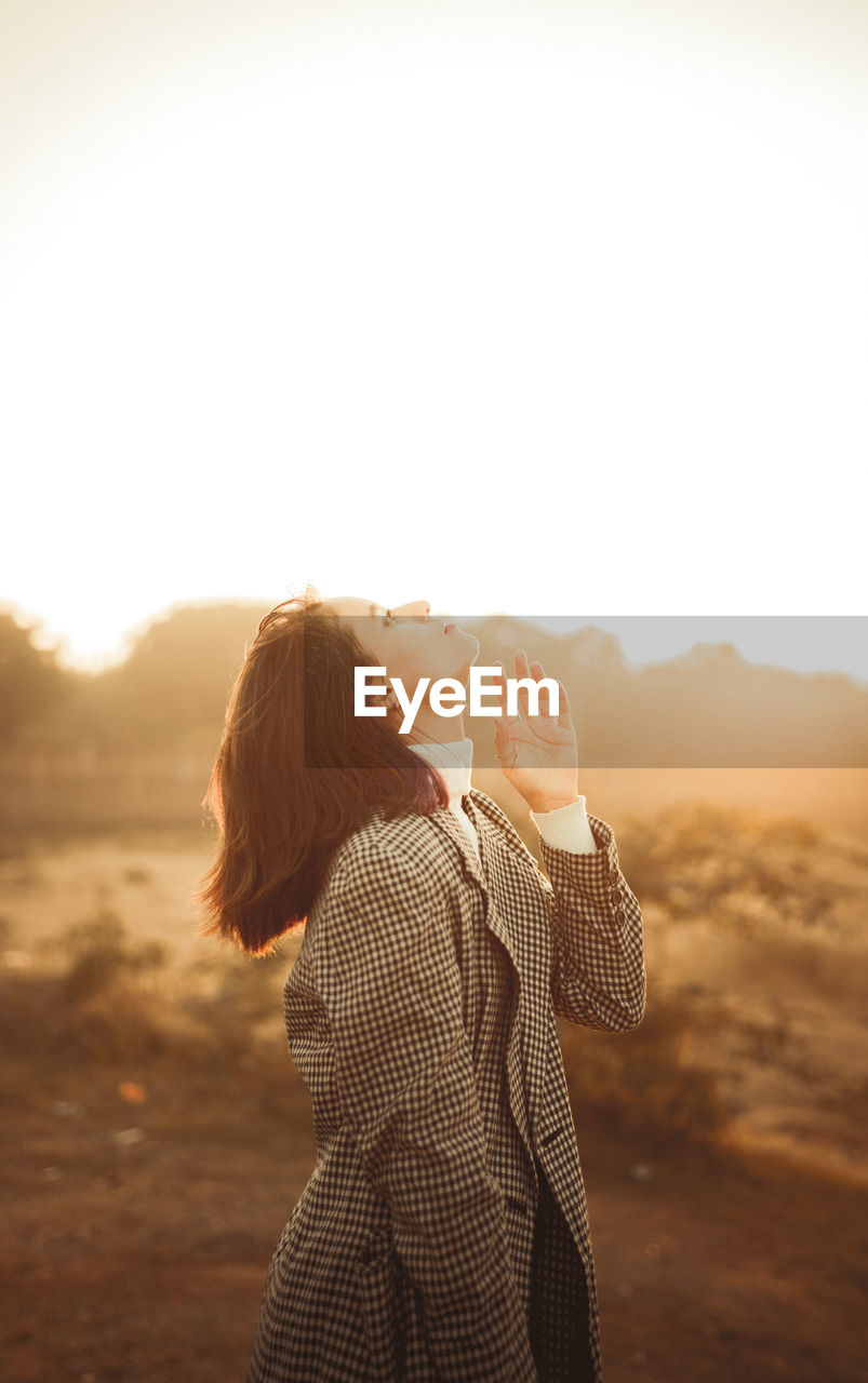 Side view of woman photographing against sky during sunset