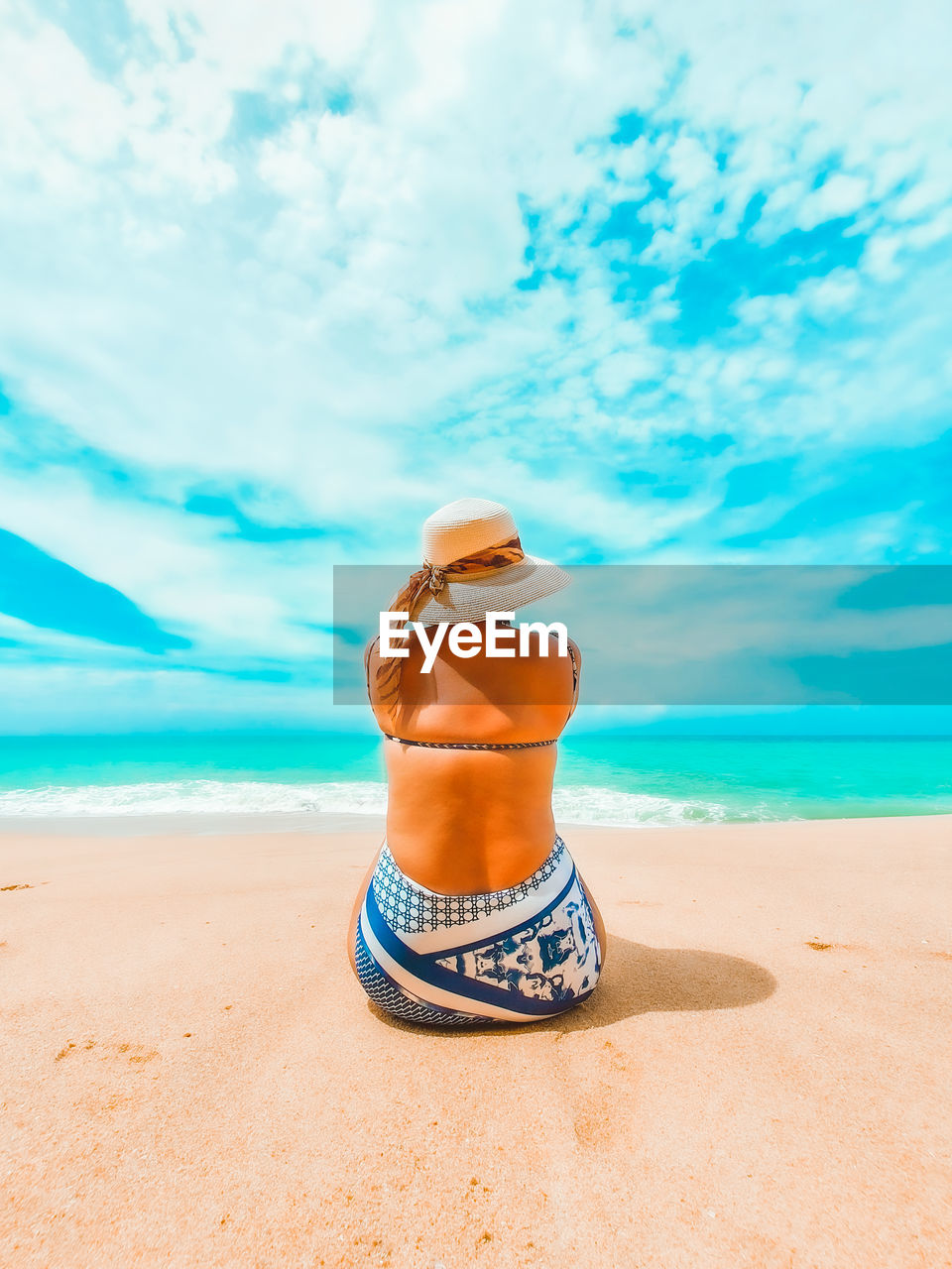 Woman wearing hat sit on the sandy beach against sky