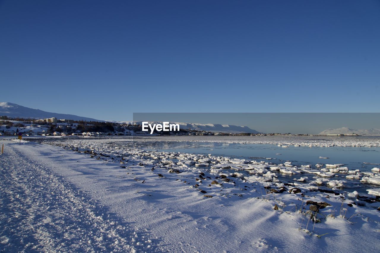 Scenic view of snow covered land against clear blue sky