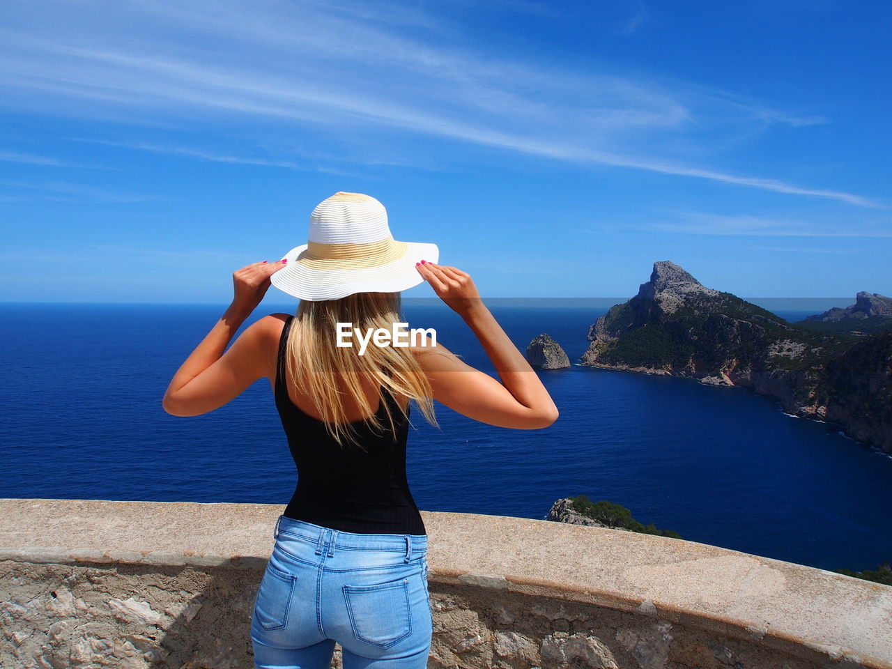 Rear view of woman standing on sea shore against blue sky