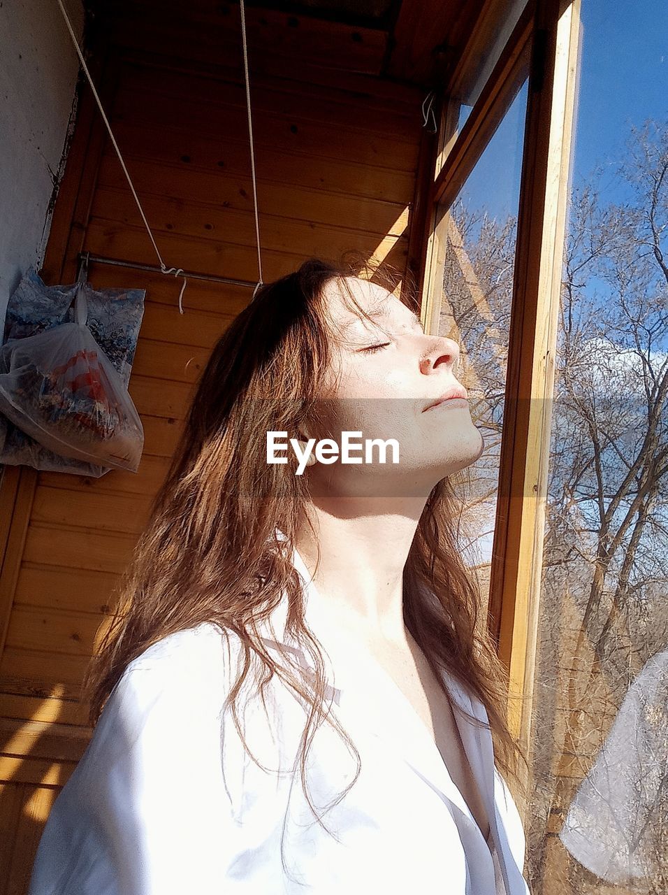 Woman with eyes closed standing by window at home