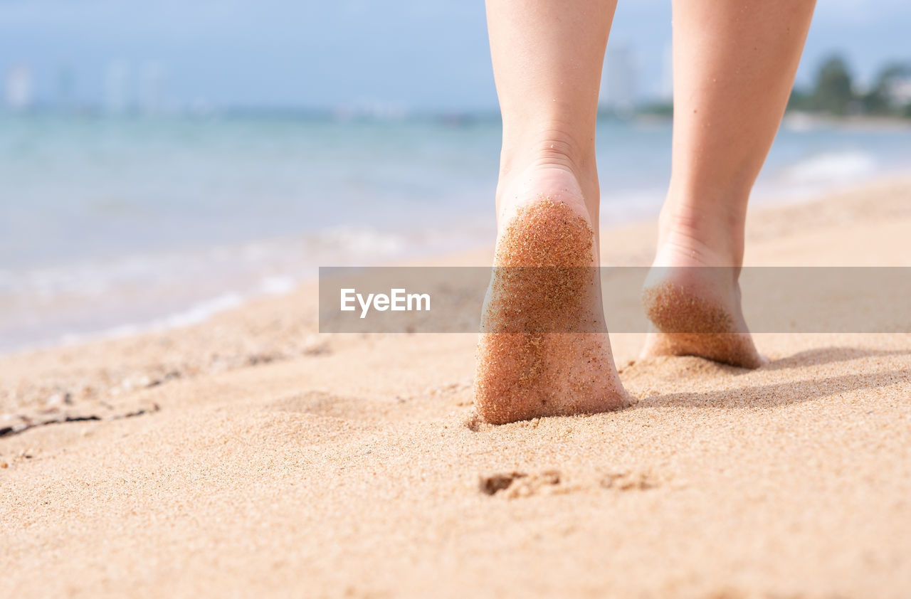 Low section of woman walking on sand at beach