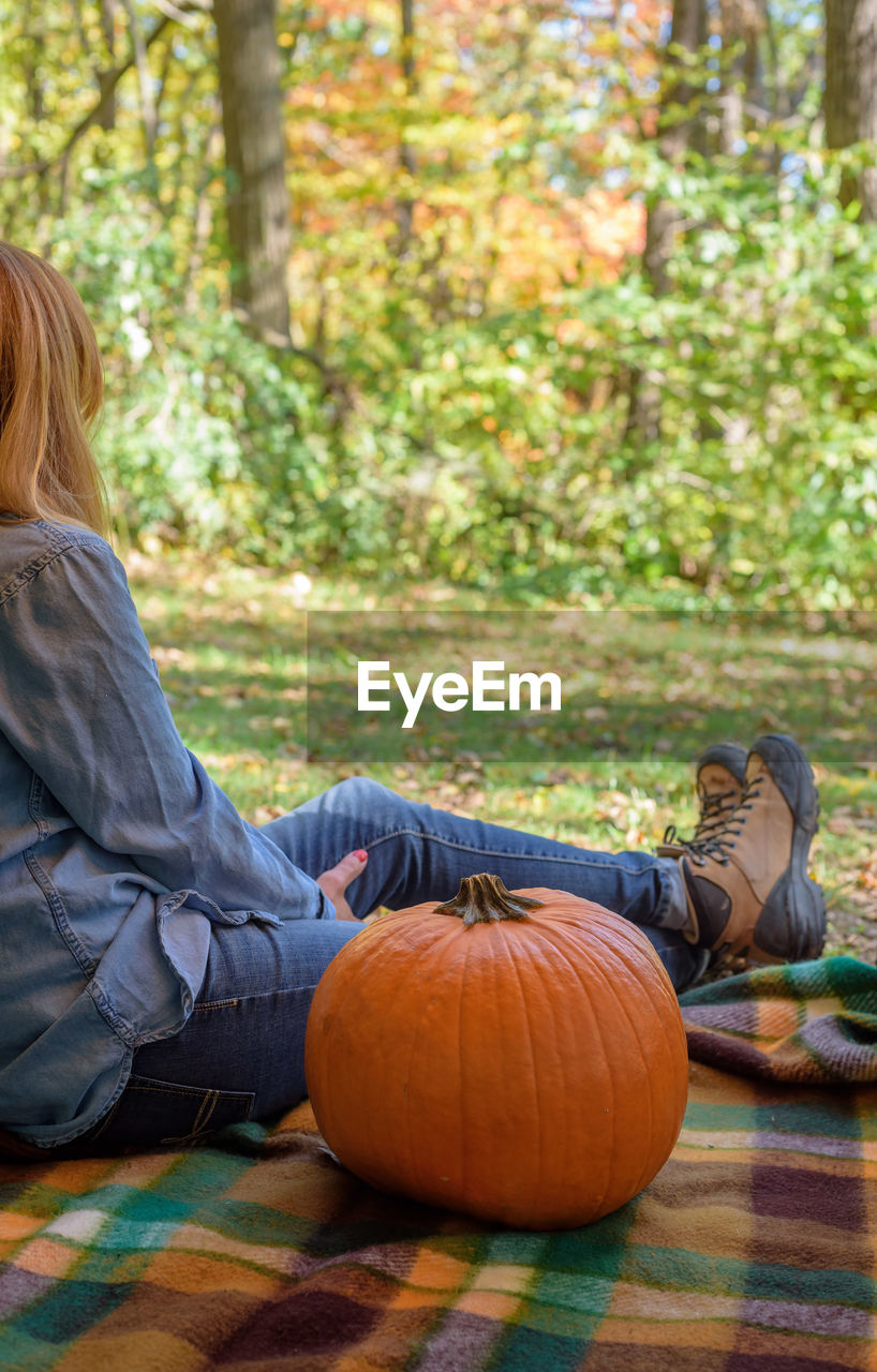 Woman with pumpkin sitting on field at park