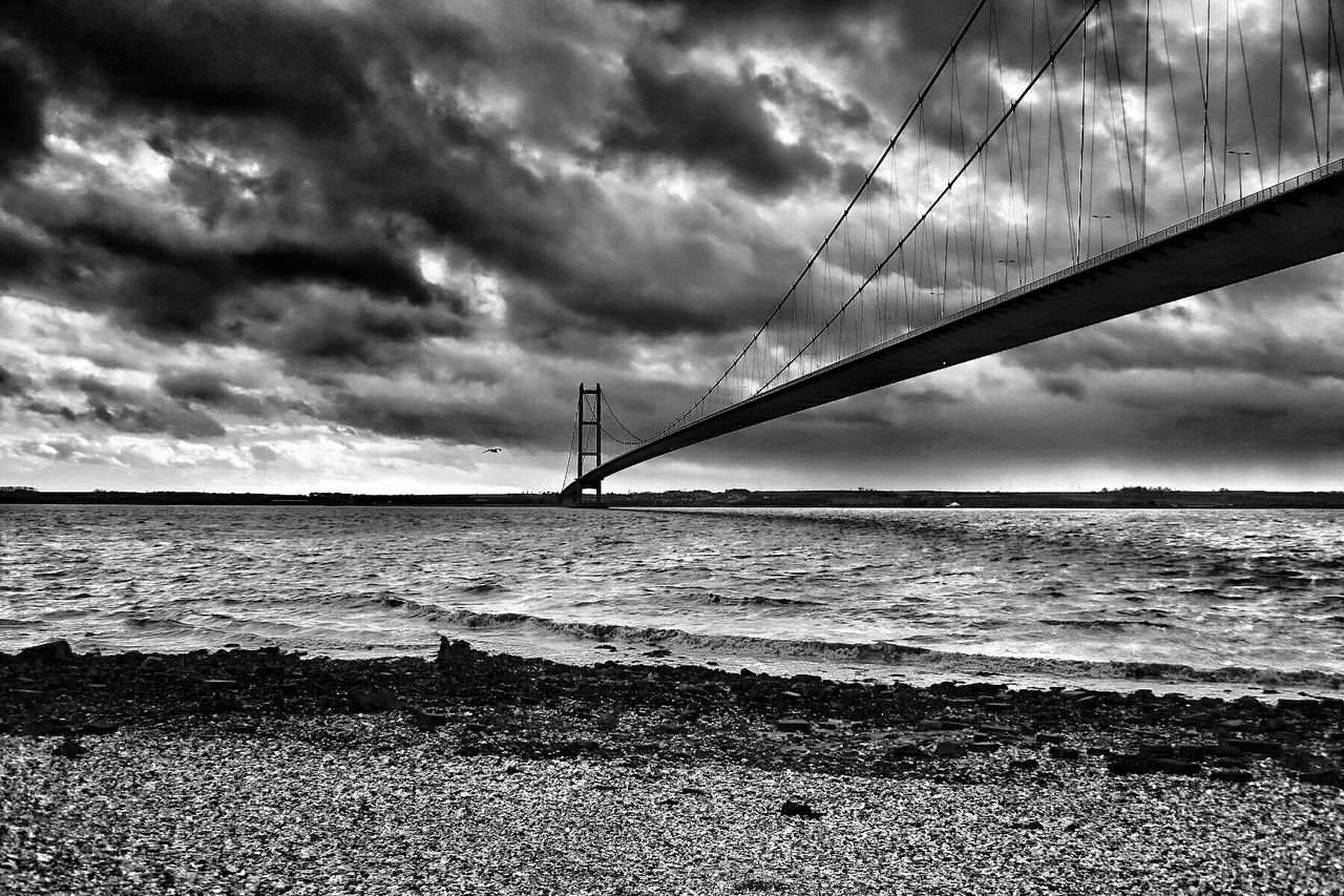 Suspension bridge over sea against cloudy sky