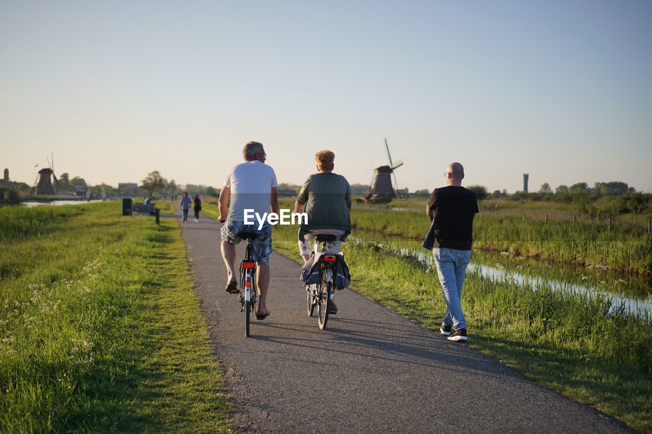 Rear view of people riding bicycles on road against clear sky at sunset