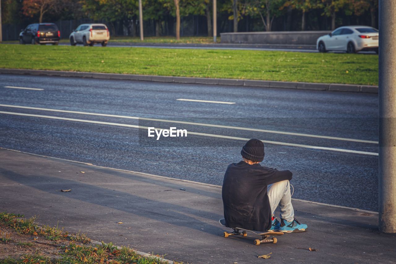 REAR VIEW OF MAN ON STREET AGAINST ROAD