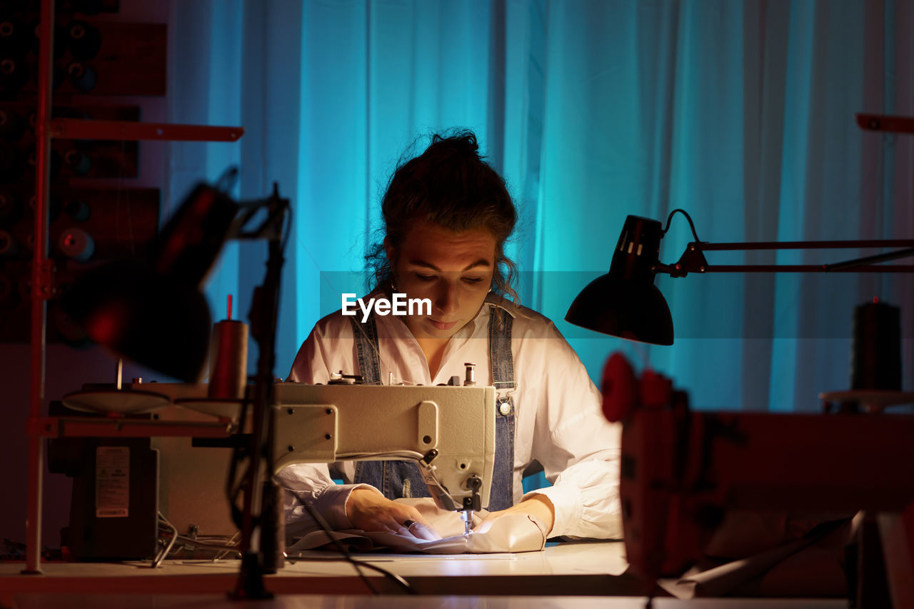 Self-employed young woman work on sewing machine in little creative atelier creating bespoke clothes