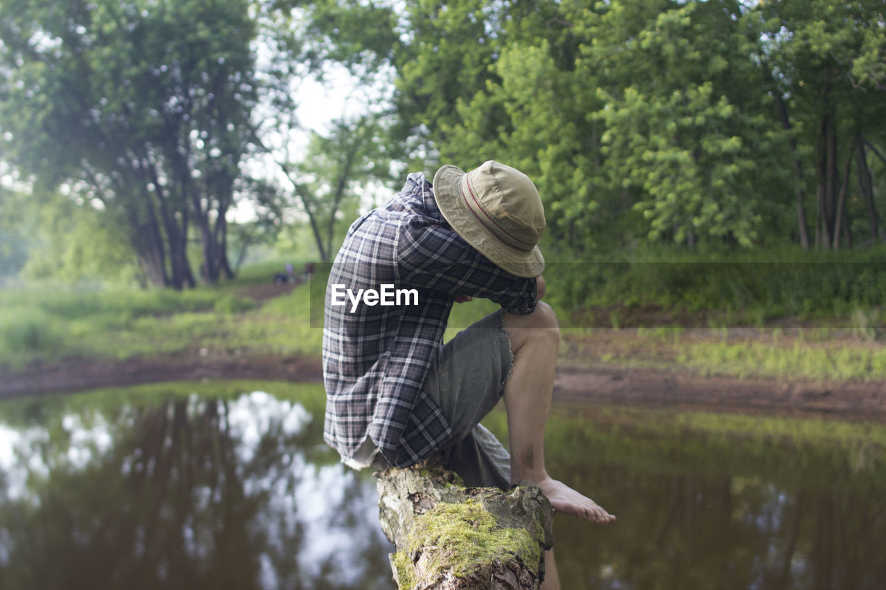 MAN STANDING BY TREE AGAINST WATER