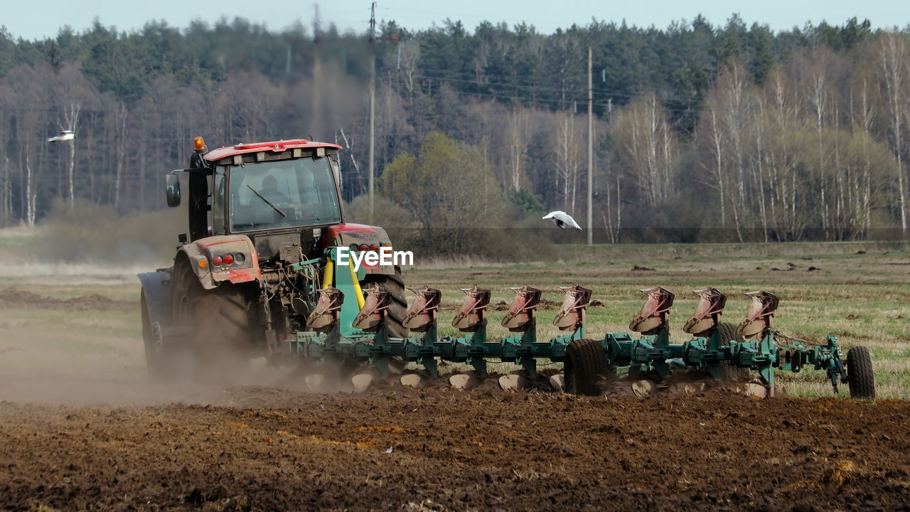 TRACTOR ON FIELD AGAINST TREES