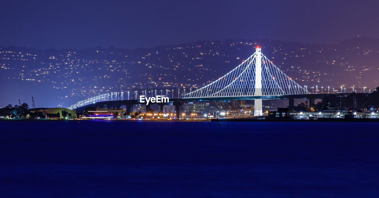 illuminated bridge over river against clear sky at night