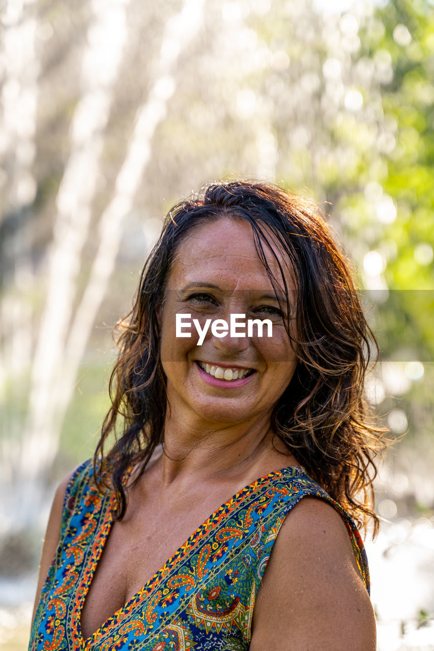 Portrait of beautiful middle aged woman in front of a fountain in a park at sunset