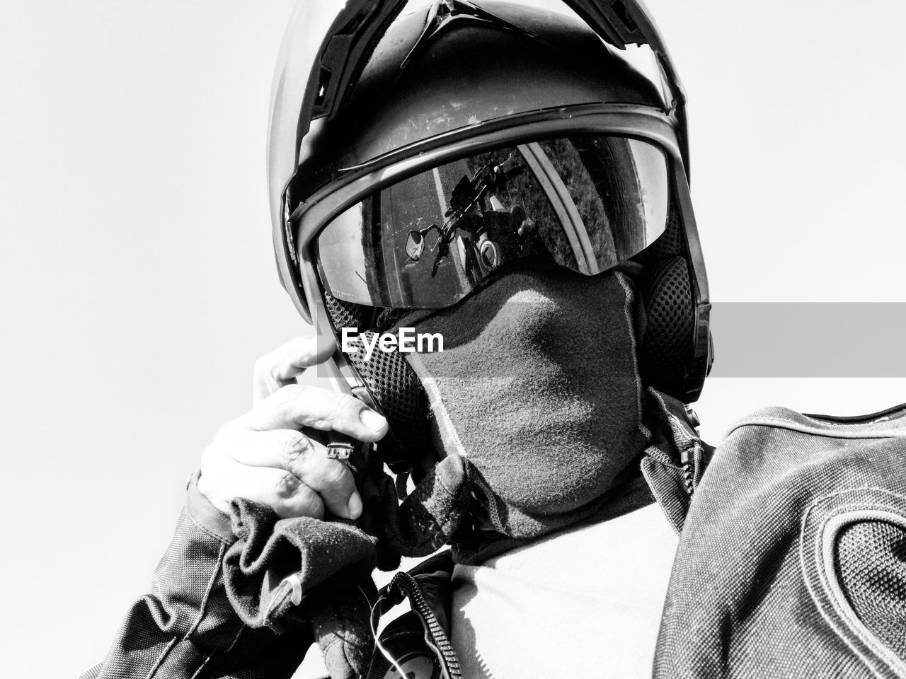 Low angle portrait of biker wearing helmet standing against clear sky