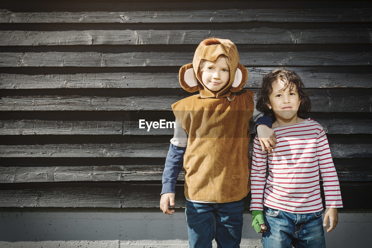 Girl in monkey suit standing with friend against black wooden wall