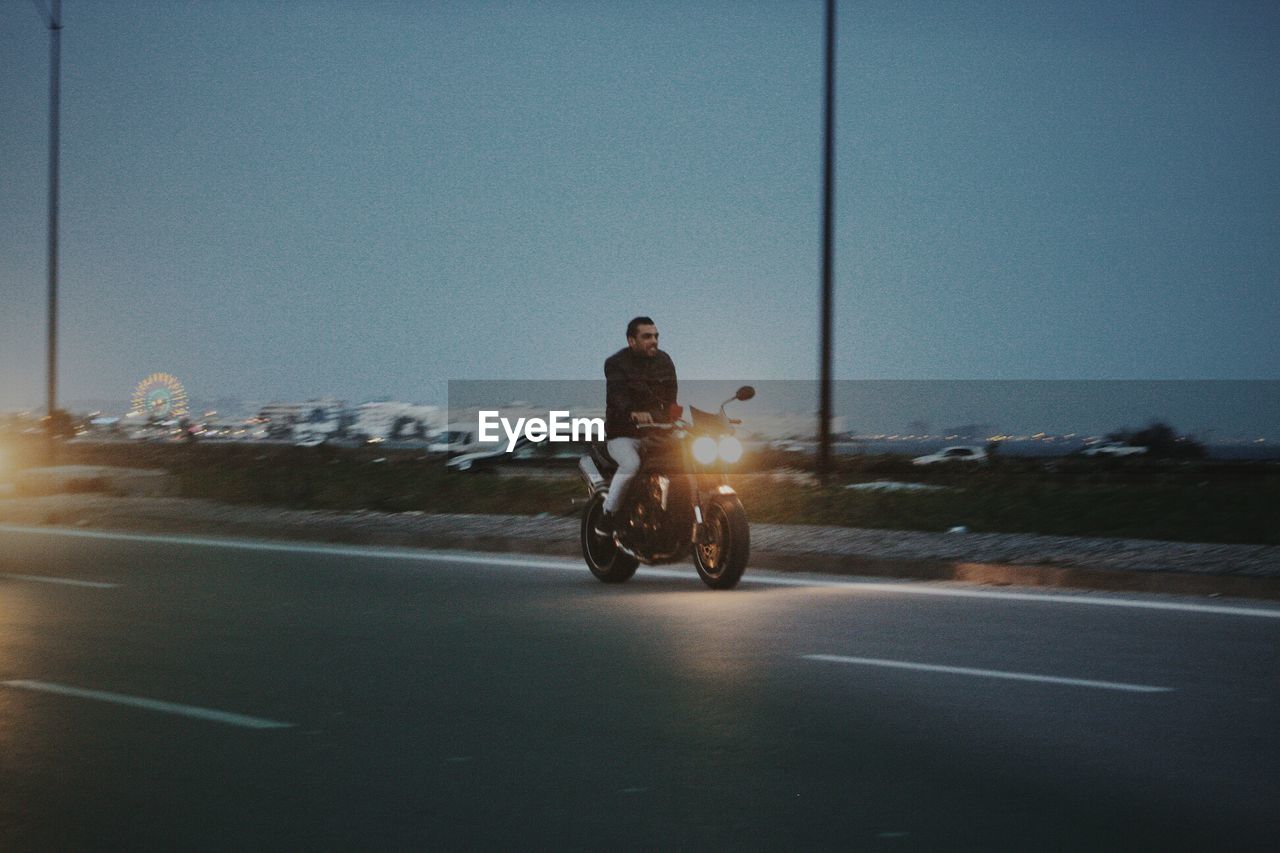Man riding motorcycle on road against sky at dusk