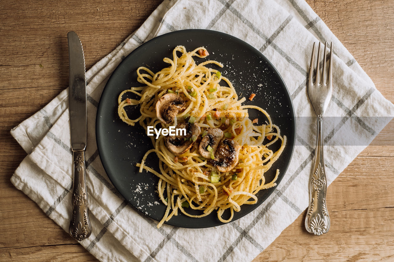 Spaghetti pasta with champignon mushrooms sprinkled with cheese parmesan on plate on wooden table