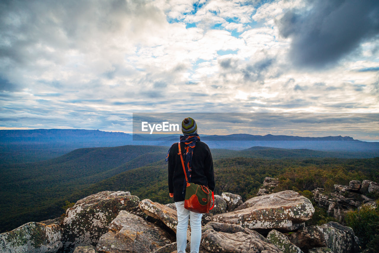 Woman standing on rocks at grampians national park against cloudy sky