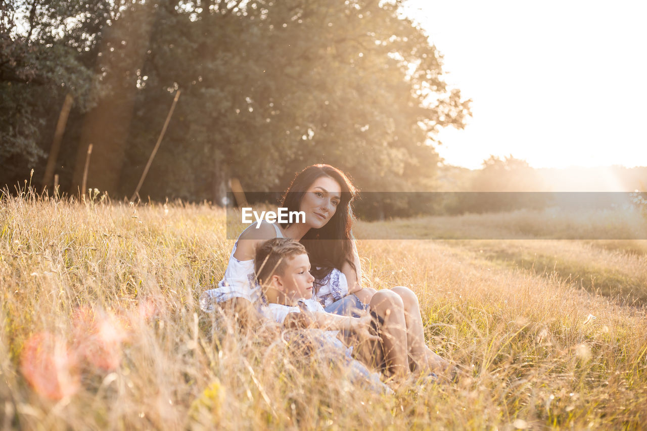 Mother and son relaxing on field in sunny day