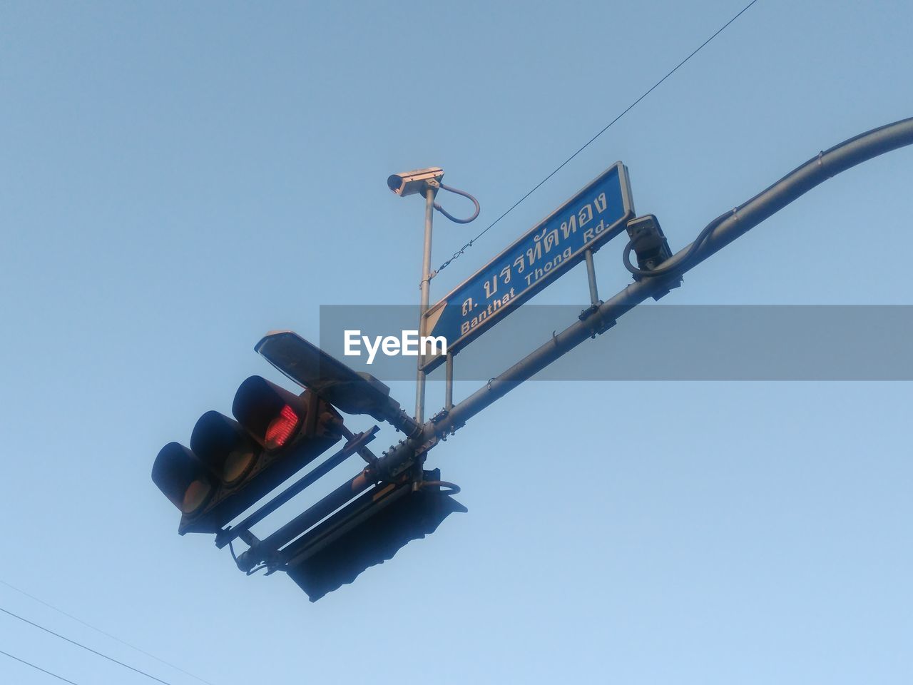 Low angle view of arrow sign and security camera against clear sky