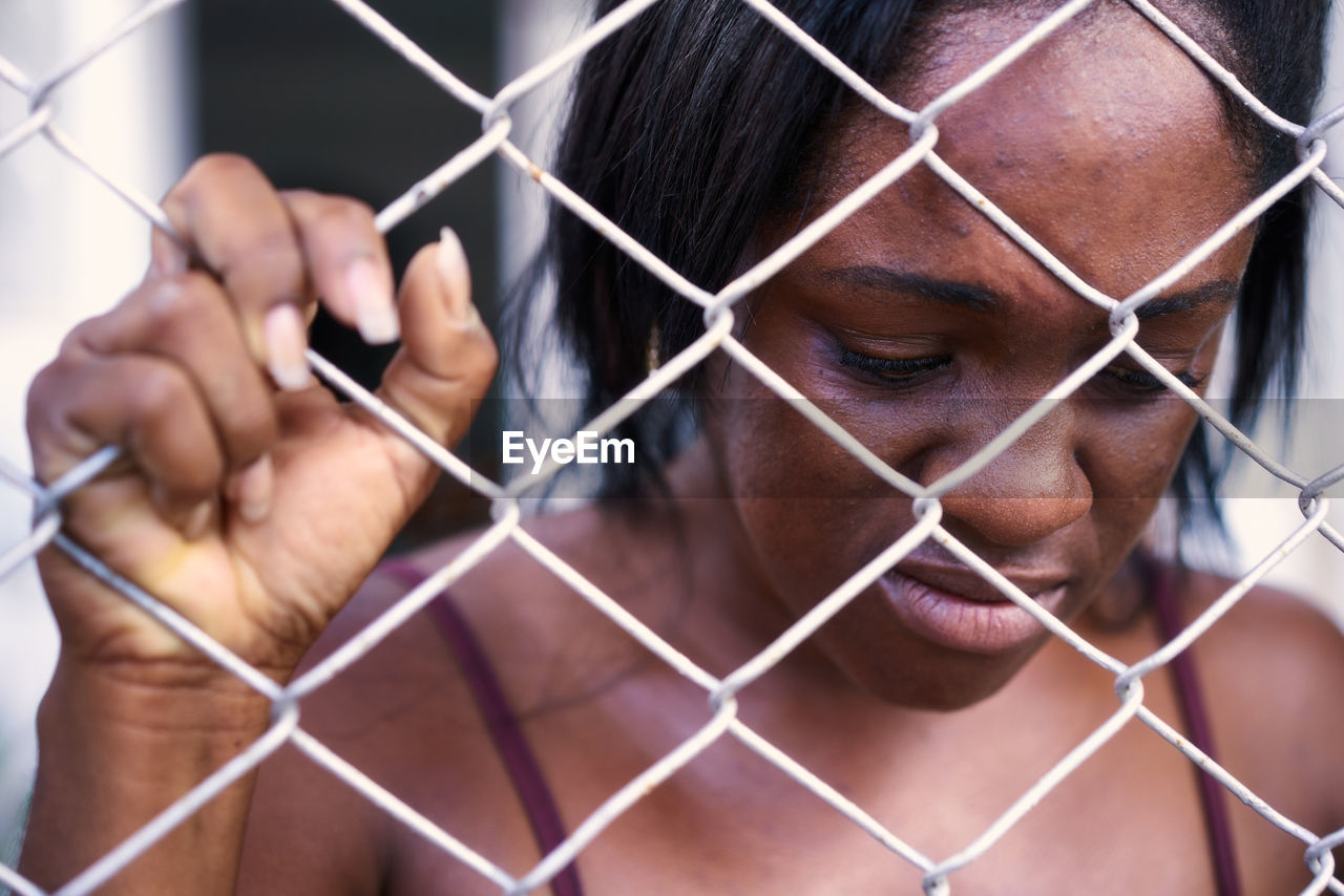 Shirtless sad woman holding chainlink fence