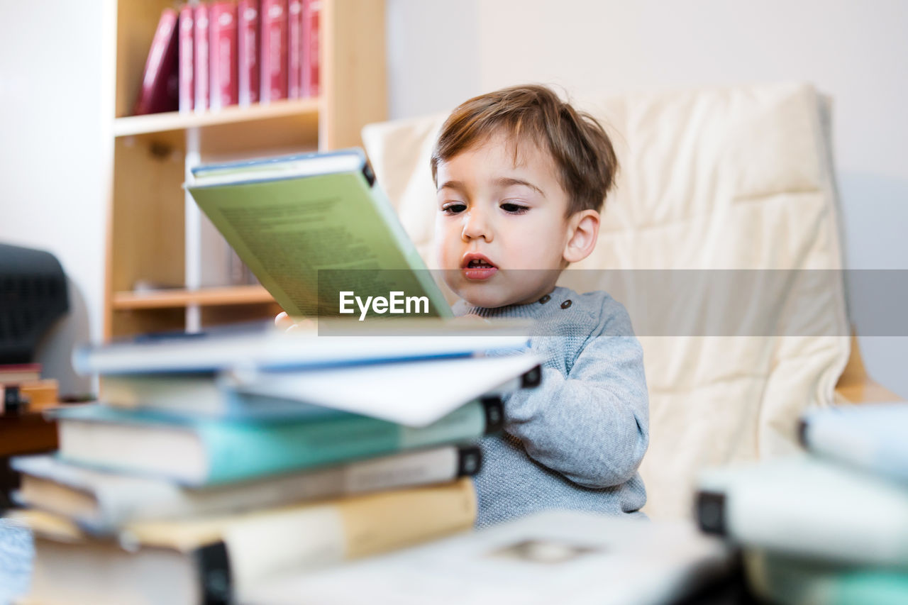 Cute boy with books on table at home