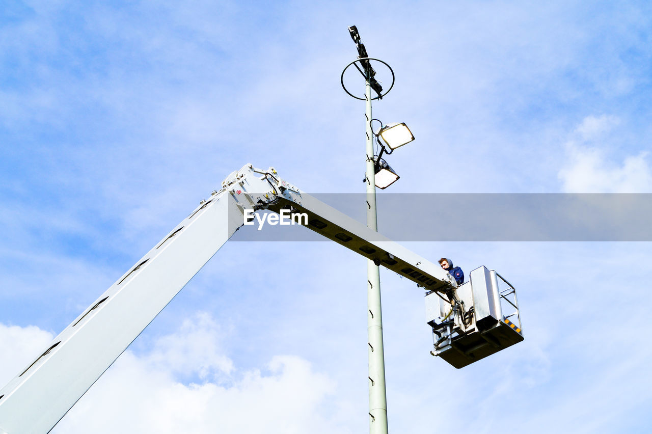 Low angle view of man standing in cherry picker against sky