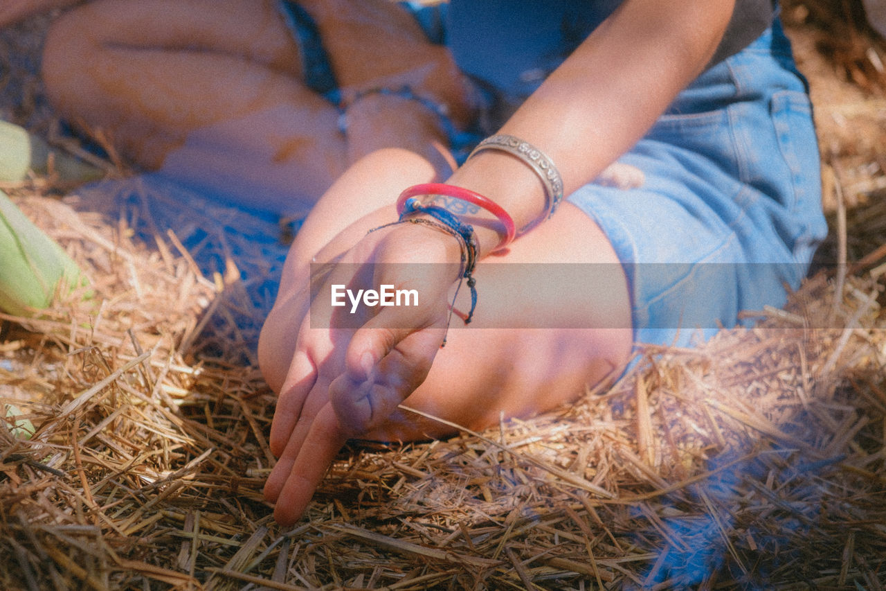 Low section of woman meditation while sitting on hay