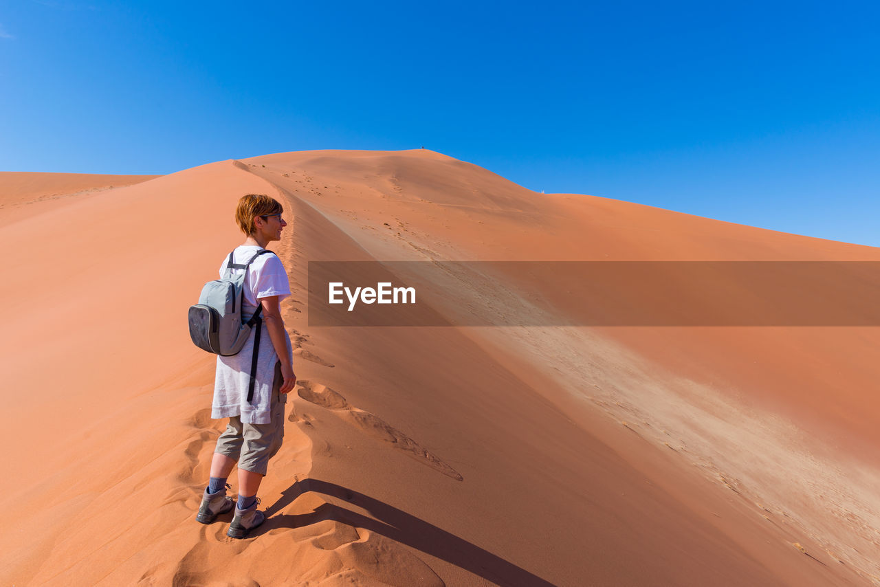 Full length of woman standing on desert against clear blue sky