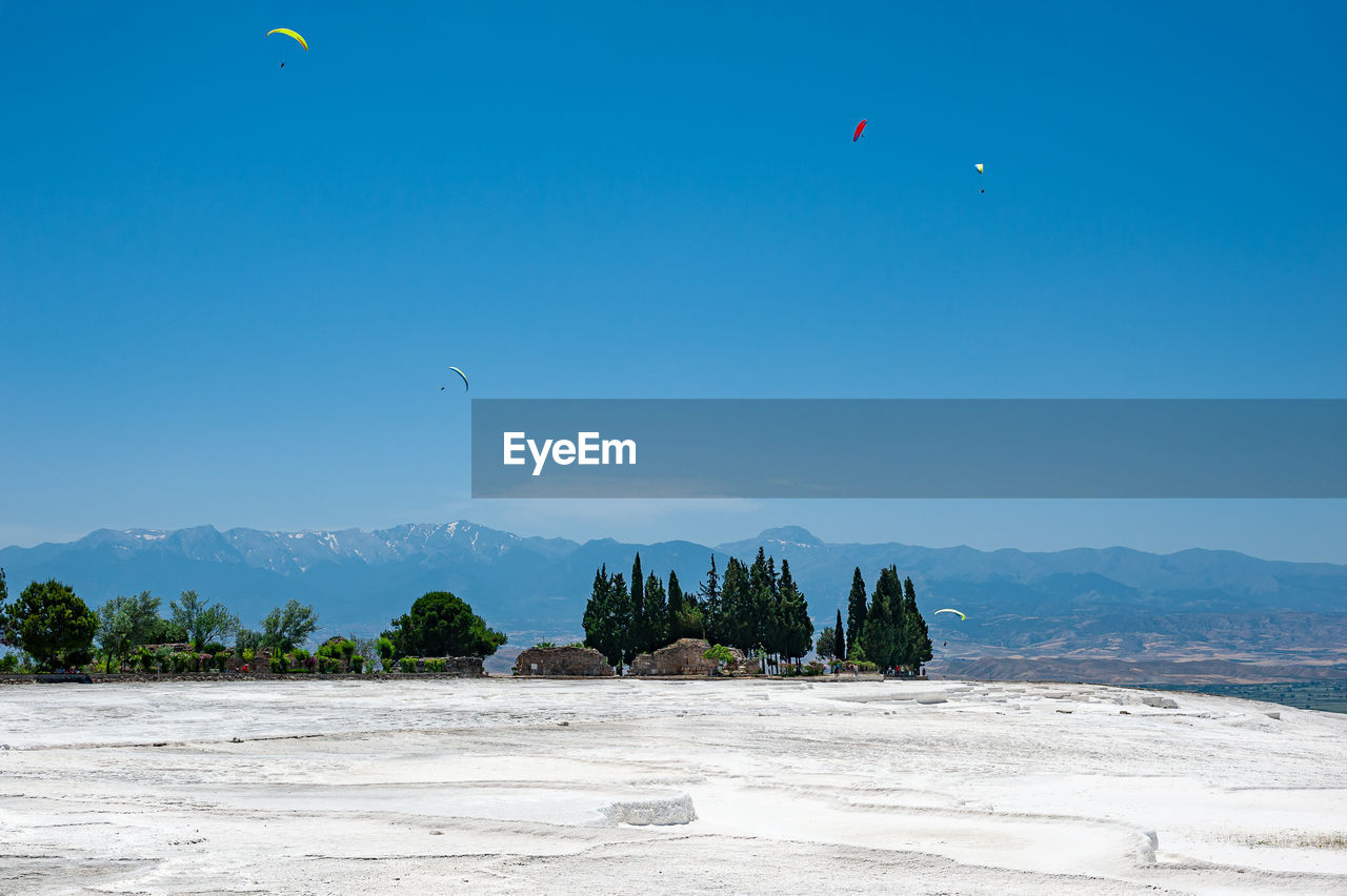 Paragliders flying above white travertines of pamukkale in an ancient city of hierapolis in turkey.