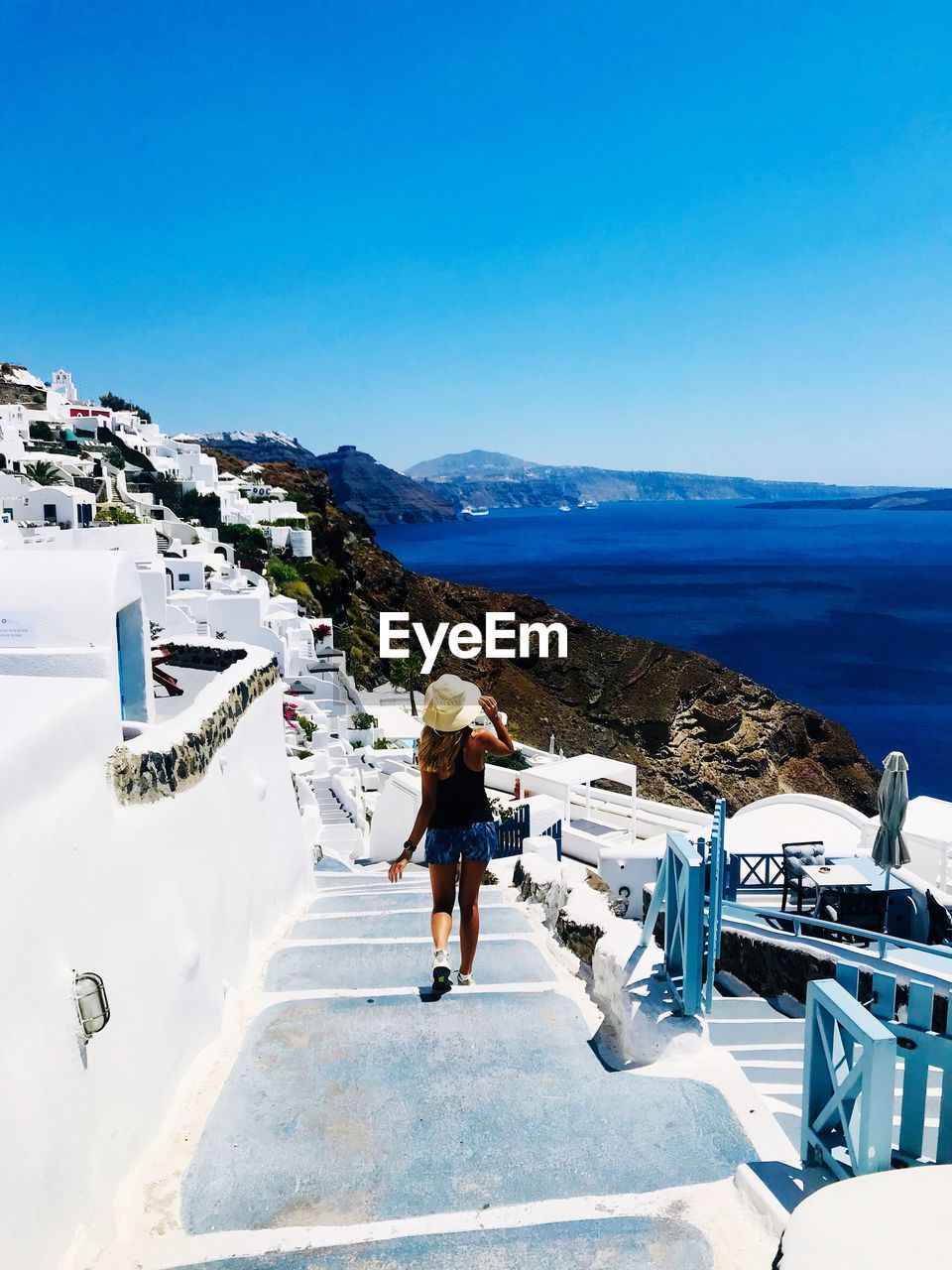 Rear view of woman walking on footpath against blue sky