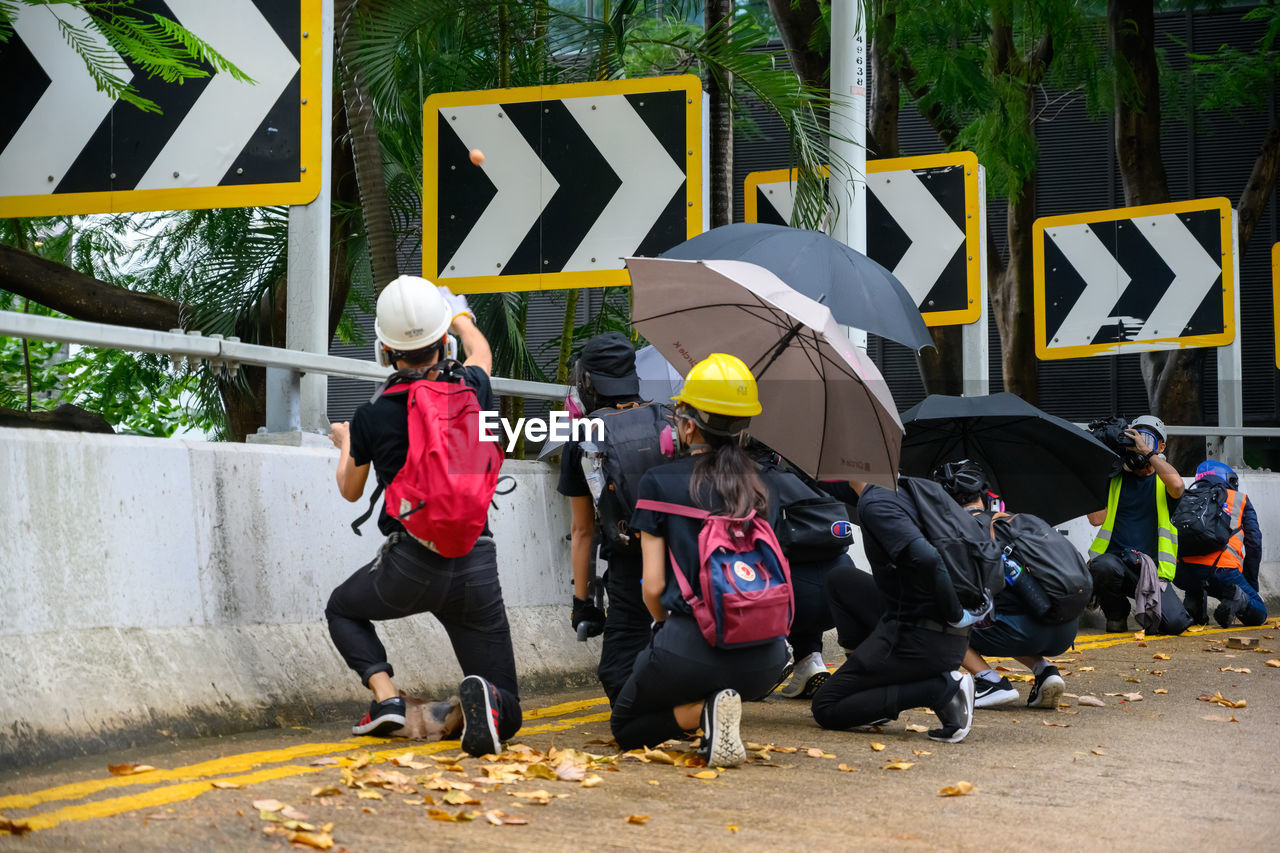 People holding umbrellas while crouching on road