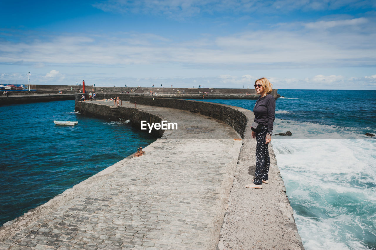 Full length of woman standing on retaining wall in sea against sky